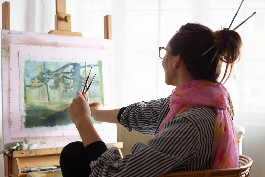 woman painting | neurofeedback for adhd in englewood, co | neurofeedback therapist in englewood, co | neurofeedback therapy for adhd in englewood, co | adhd therapy for adults in englewoods, co | adhd neurofeedback | 80126 | 80129 | 80130 Image of a happy woman painting a forest picture on canvas. Discover how neurofeedback therapy for ADHD in Englewood, CO can help you effectively manage your symptoms.