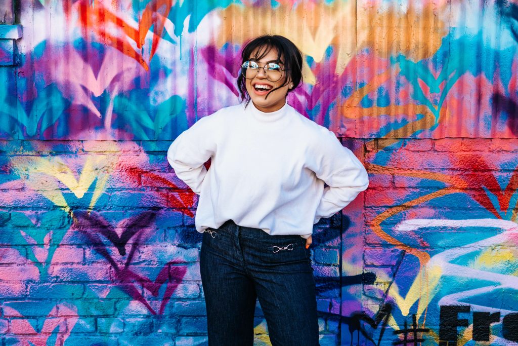 colorful mural | emdr therapy in englewood, co | emdr therapy in littleton, co | emdr therapy in greenwood village, co | emdr colorado | emdr therapy in denver | emdr trauma therapy | 80127 | 80128 | 80124 Image of a smiling woman wearing glasses standing in front of a colorful mural. Learn how effective EMDR therapy in Denver, CO can be when it comes to managing your trauma symptoms.