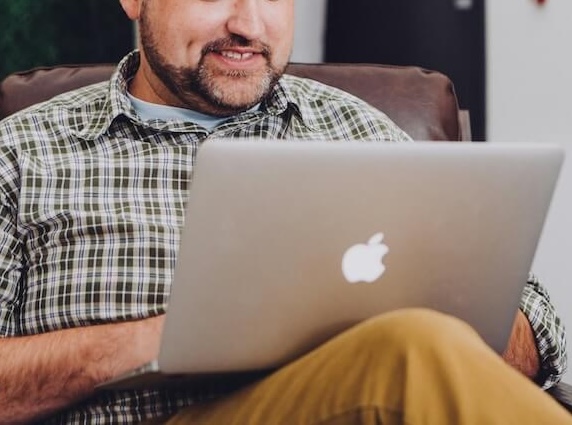 smiling man | telehealth therapy in colorado | telehealth in englewood, co | online therapy in colorado | telehealth in littleton, co | online therapy for college students | emdr therapy colorado | 80126 | 80129 | 80130 Image of an middle aged man sitting in a recliner, smiling and using a laptop. Looking for effective ways to cope with anxiety, trauma, and more? Learn how telehealth therapy in Colorado can help!