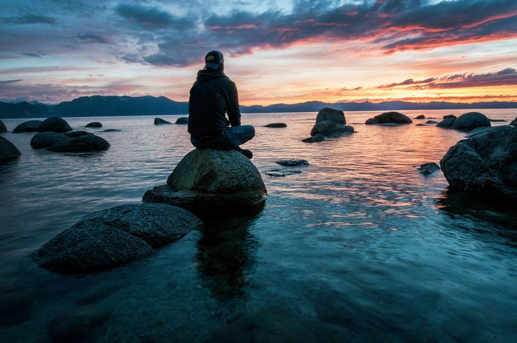 man on rock | neurofeedback for anxiety | neurofeedback therapy in denver, co | neurofeedback therapy for anxiety | neurofeedback therapist | 80125 | 80121 | 80110 Image of a man sitting on a rock in a lake looking at the sunrise. Meet with a neurofeedback therapist to start managing your anxiety symptoms. Learn how neurofeedback for anxiety can help you!