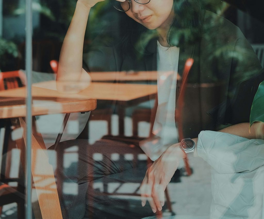 woman at table | emdr therapy in denver, co | emdr therapist in denver, co | emdr trauma therapy | emdr for ptsd | online therapy in colorado | 80127 | 80128 | 80124 Image of an upset woman behind a window sitting at a table in a cafe. Learn how EMDR therapy in Denver, CO can help you cope and work to improve your trauma symptoms.