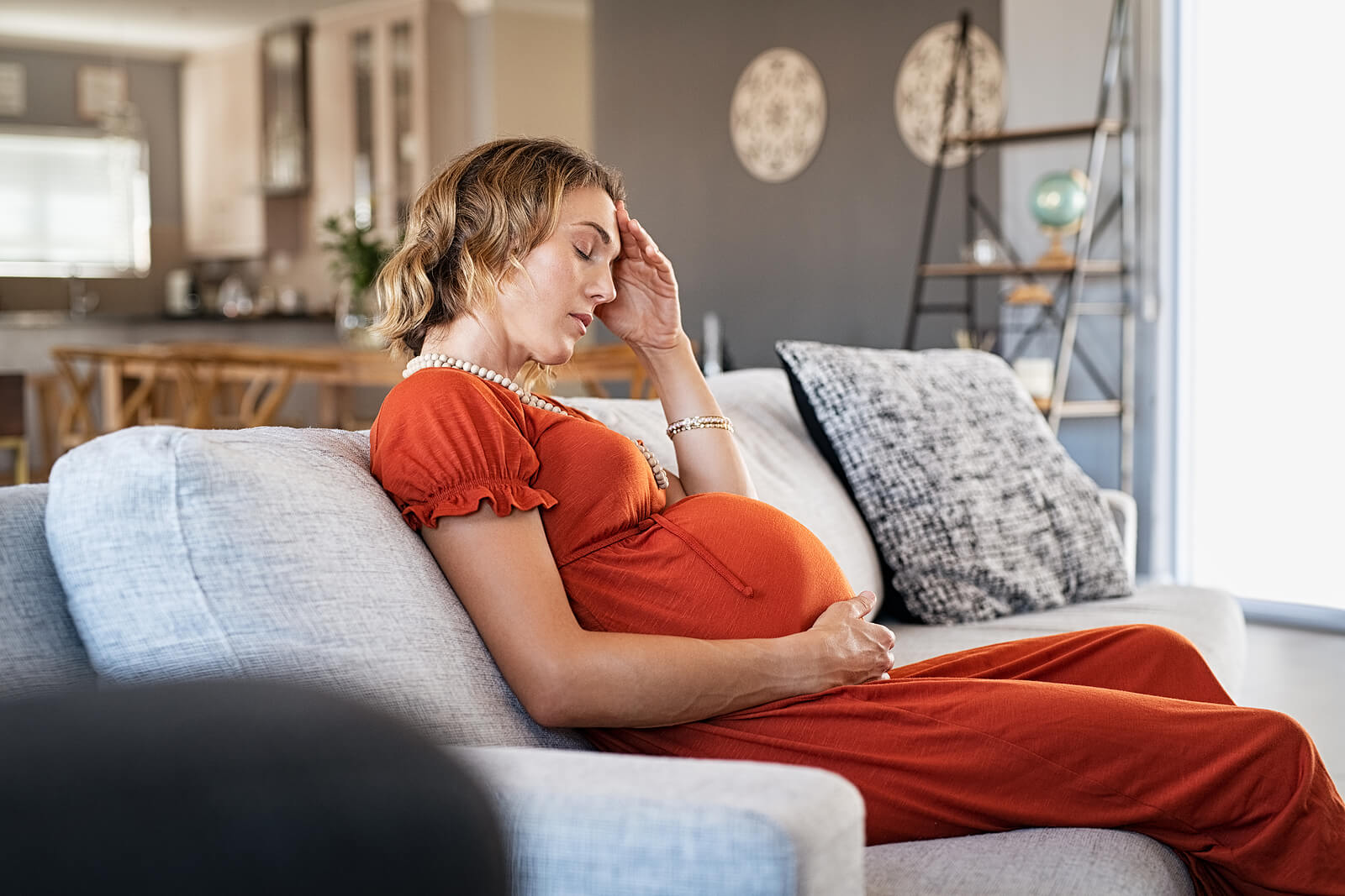 stressed and pregnant | postpartum therapist | postpartum depression counseling in englewood, co | trauma therapist in englewood, co | englewood, co | greenwood village, co | denver, co A visibly stressed pregnant woman sits on a couch at home, resting her head in her hand. Prenatal anxiety and emotional distress are common, and postpartum depression counseling in Englewood, CO can provide vital support before and after birth.